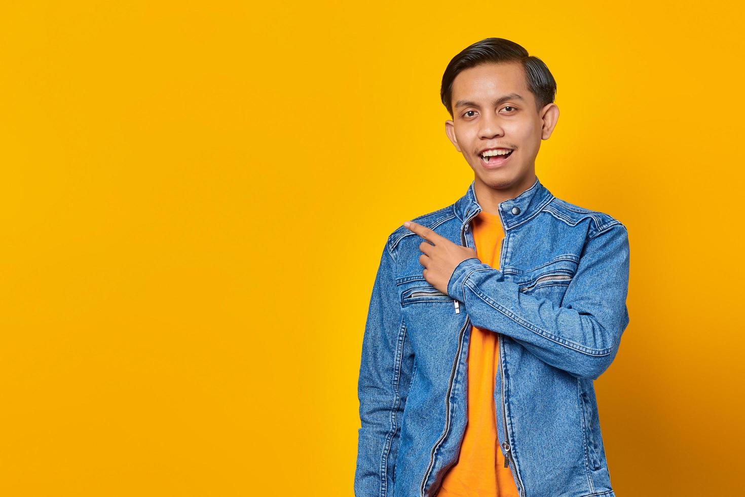 Portrait of a cheerful and excited Asian man pointing to an empty space isolated on yellow background photo