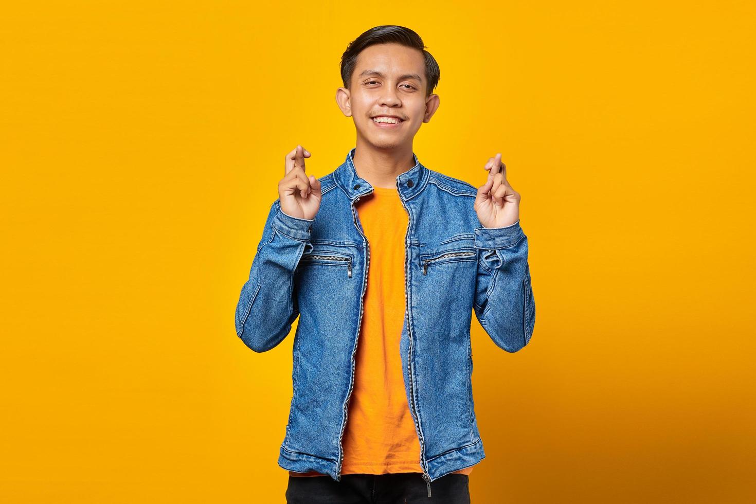 Portrait of smiling young asian man uniform gesturing finger crossed on yellow background photo