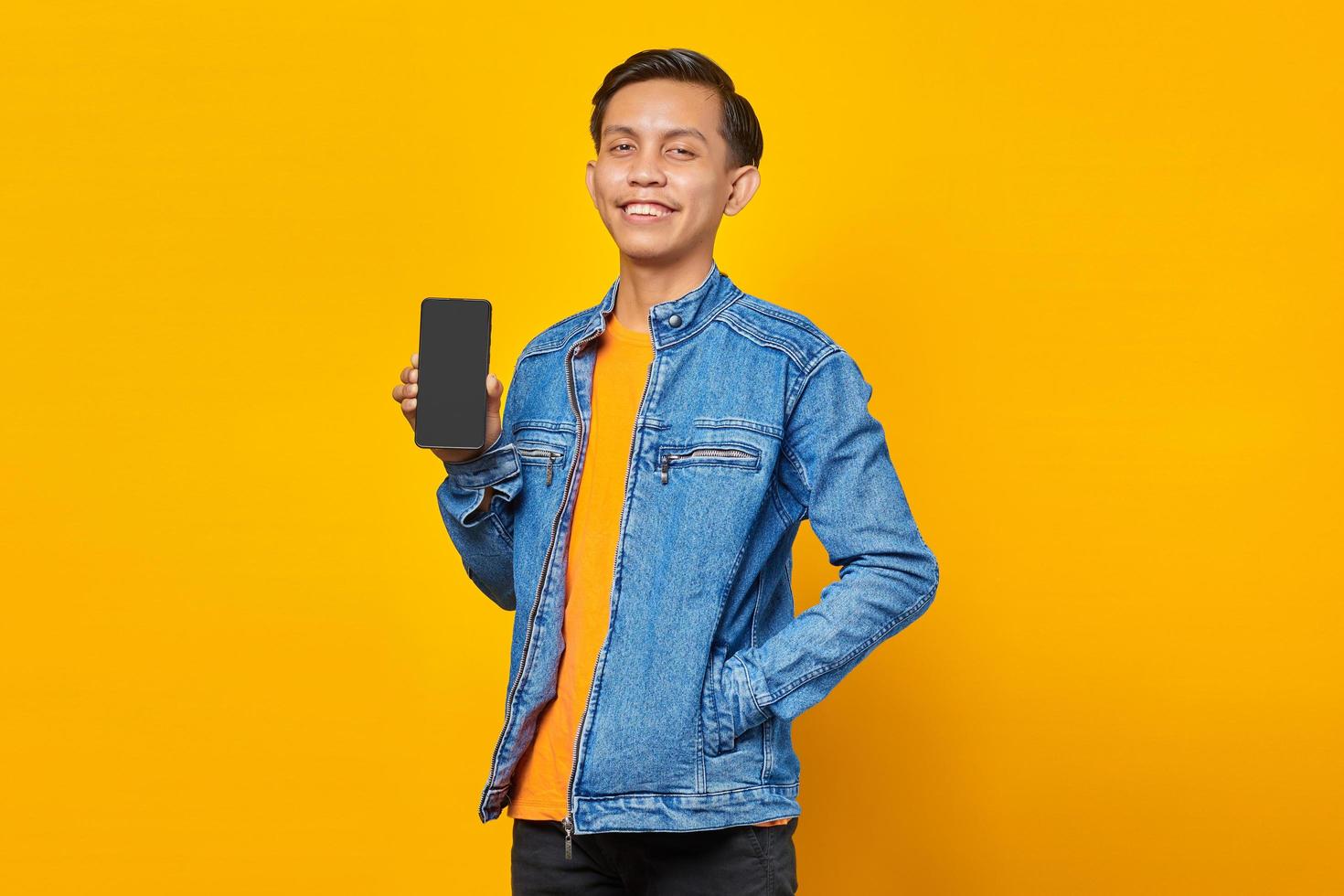 Portrait of smiling young asian man showing smartphone isolated on yellow background photo