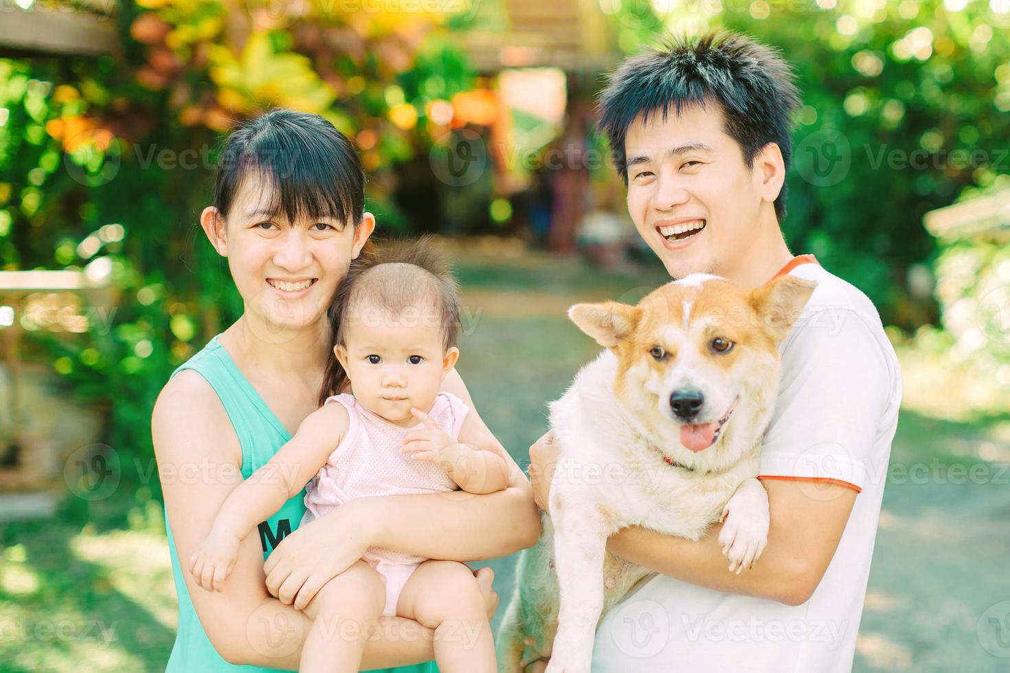 Retrato de padres de familia asiáticos y un bebé que sonríe junto con su perro en el jardín. foto