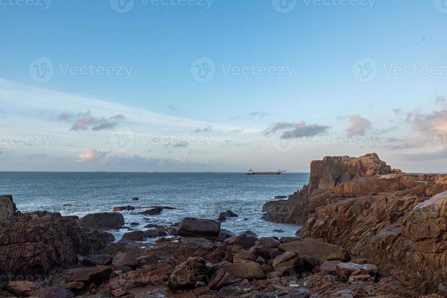 In the morning, the sun shines on the rocks and waves on the beach photo