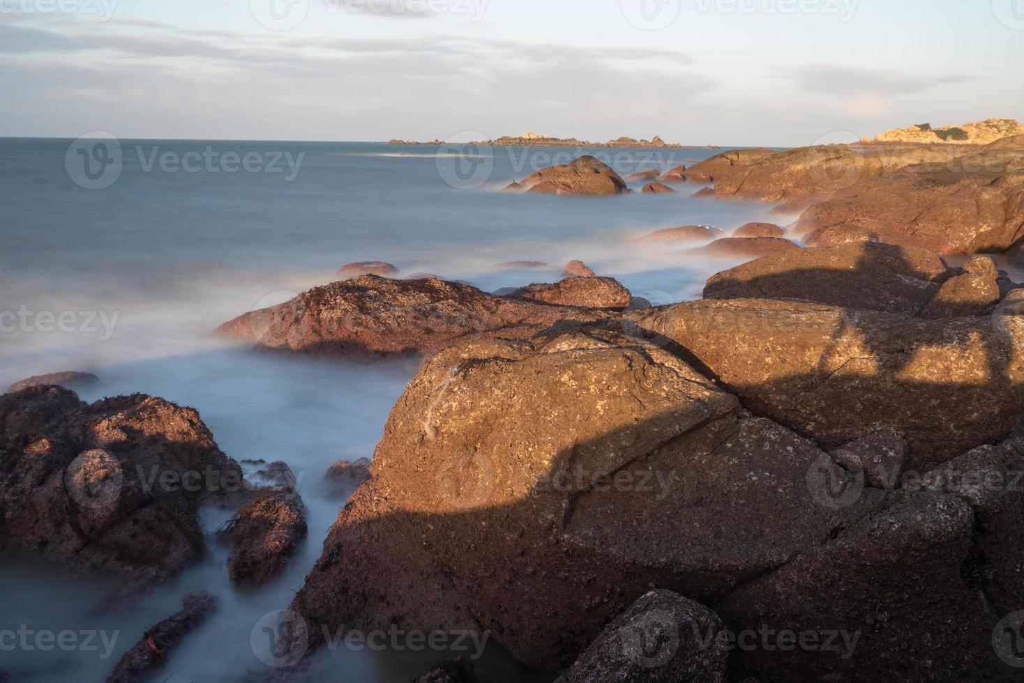 In the morning, the sun shines on the rocks and waves on the beach photo