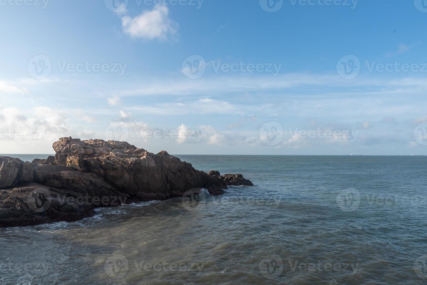 In the morning, the sun shines on the rocks and waves on the beach photo