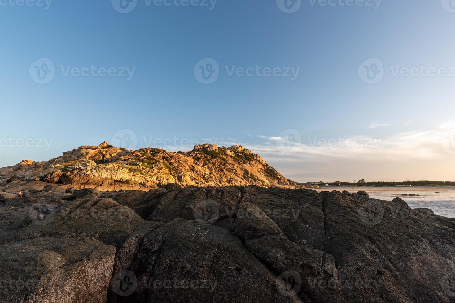 In the morning, the sun shines on the rocks and waves on the beach photo