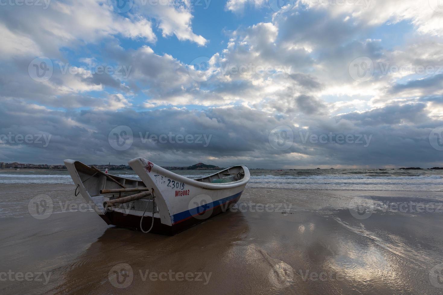 un pequeño bote atracado en la playa nublada, y el cielo estaba cubierto de nubes oscuras foto