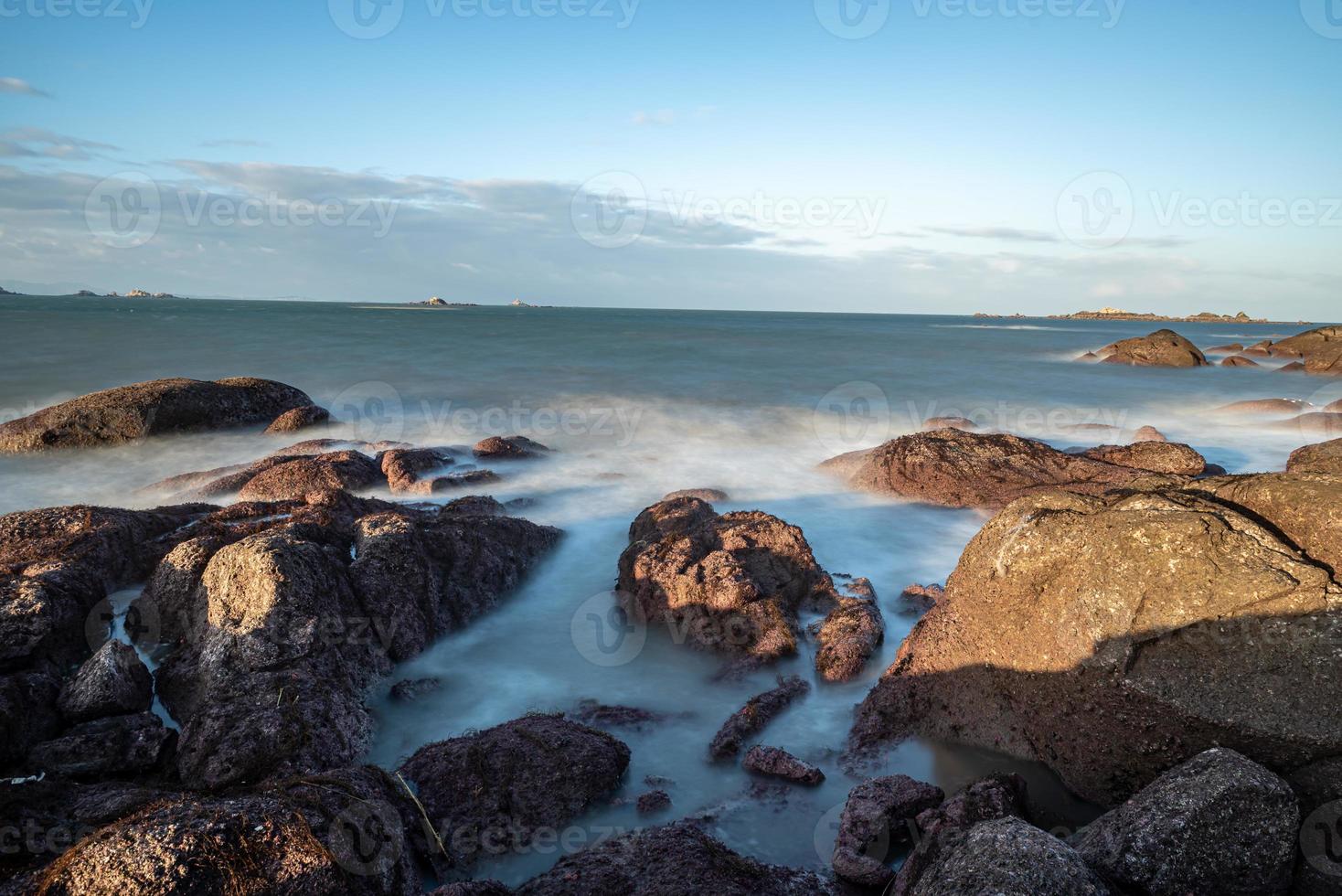 In the morning, the sun shines on the rocks and waves on the beach photo