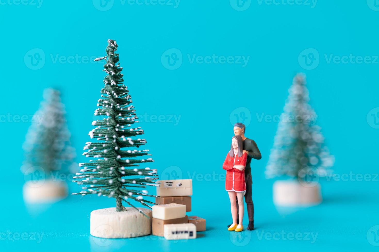 Gente en miniatura, pareja de enamorados de pie junto a un árbol de navidad foto
