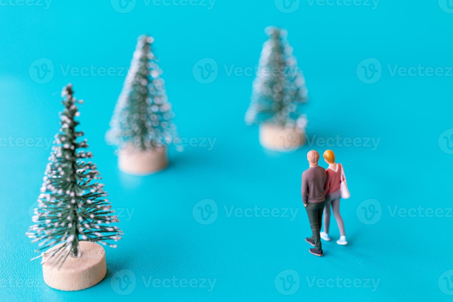 Gente en miniatura, pareja de enamorados de pie junto a un árbol de navidad foto