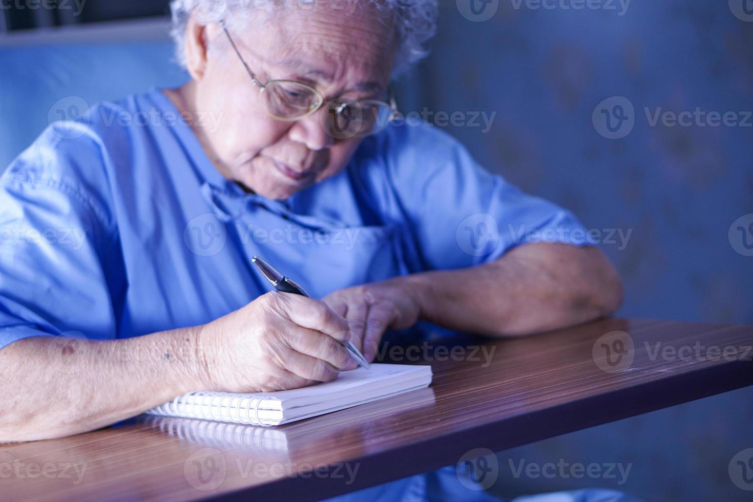 Asia anciana o anciana mujer paciente escribiendo mientras está sentado en la cama en la sala del hospital de enfermería, concepto médico fuerte y saludable foto