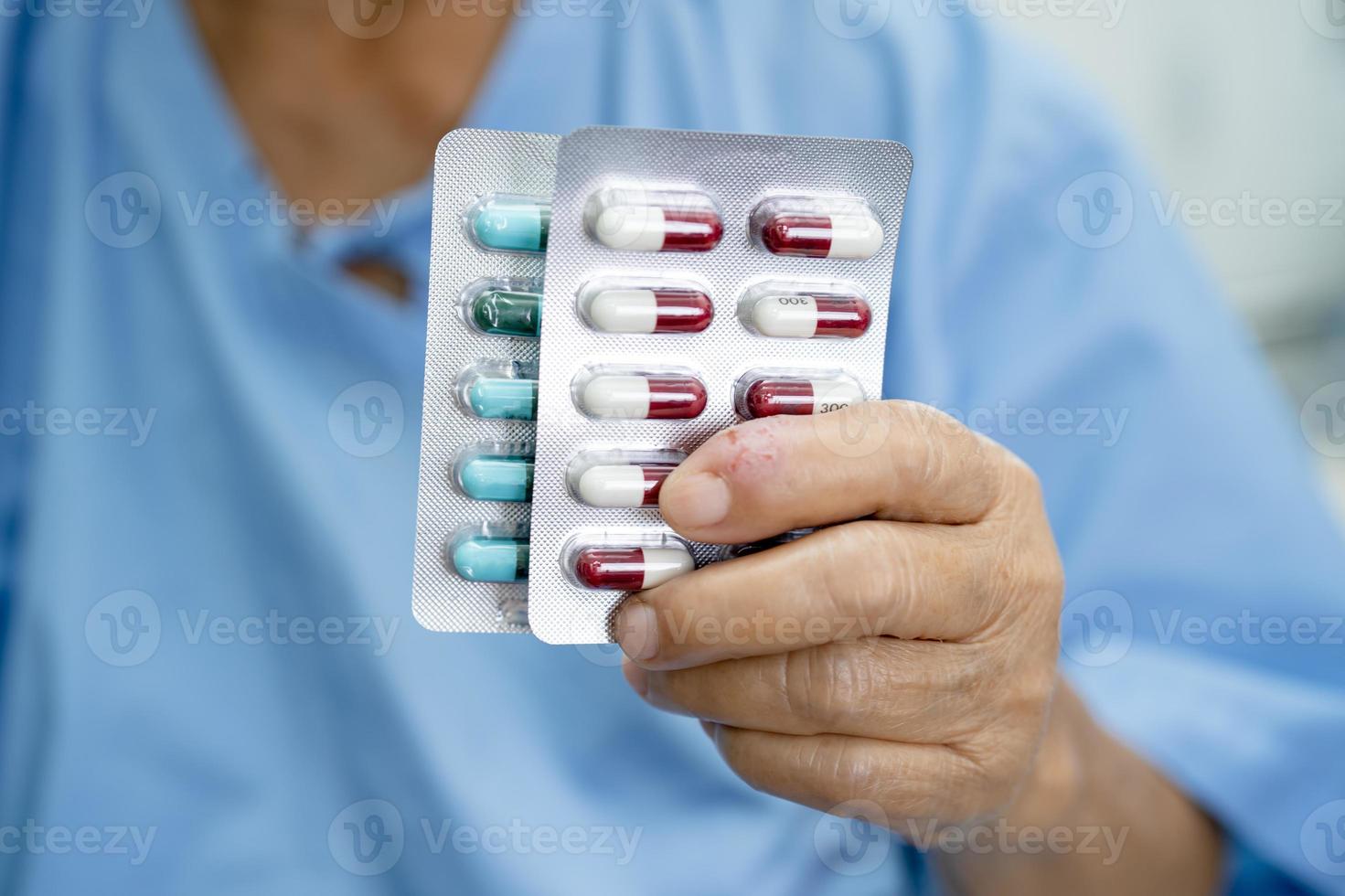 Asian senior woman patient holding antibiotics capsule pills in blister packaging for treatment infection patient in hospital, Pharmacy drugstore concept. Pharmacy drugstore concept. photo