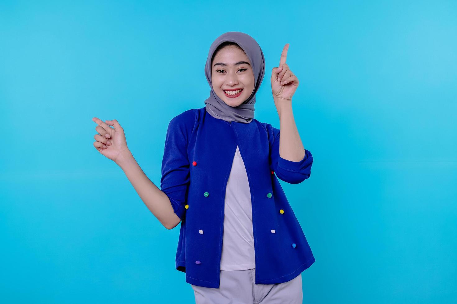 Good looking charismatic young woman with wearing hijab pointing isolated on light blue background photo