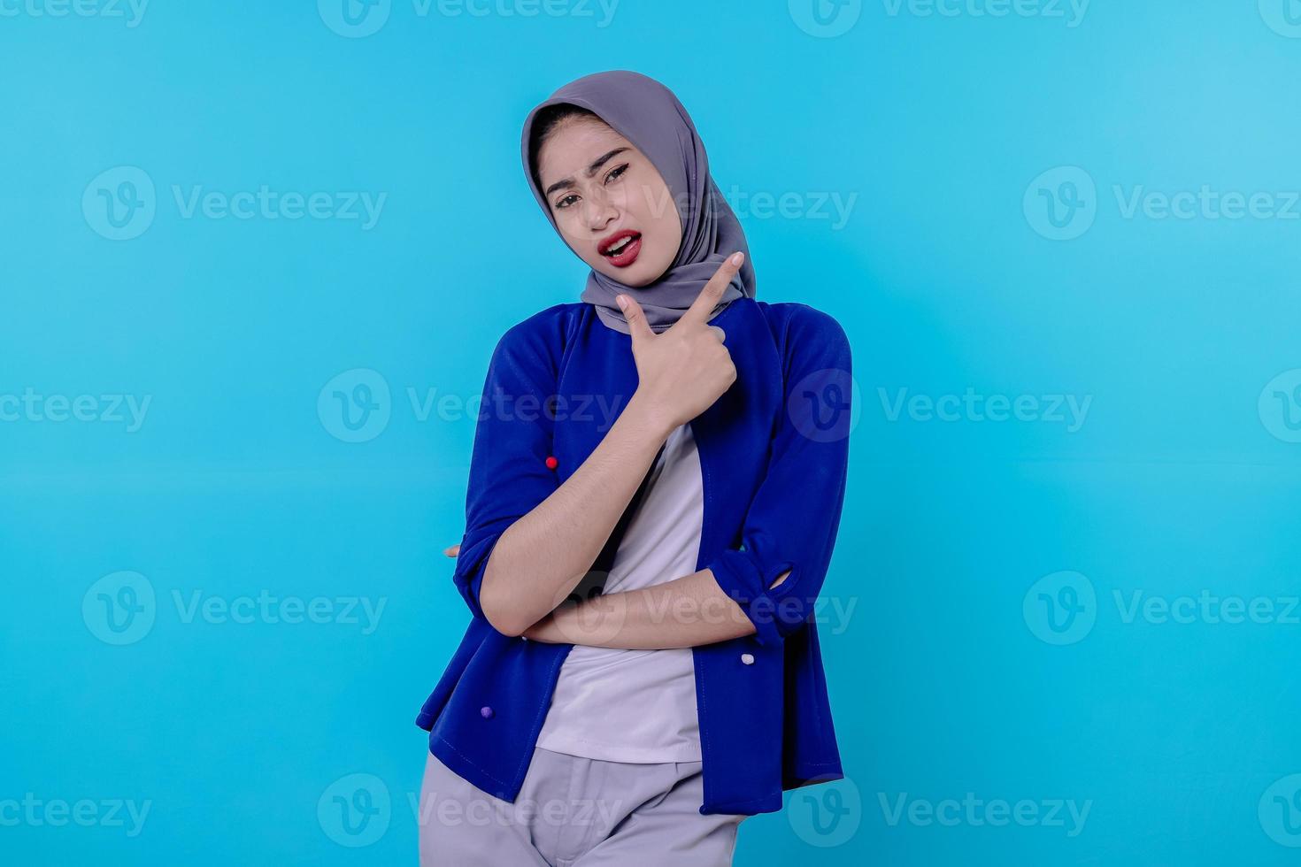 Good looking charismatic young woman with wearing hijab pointing isolated on light blue background photo