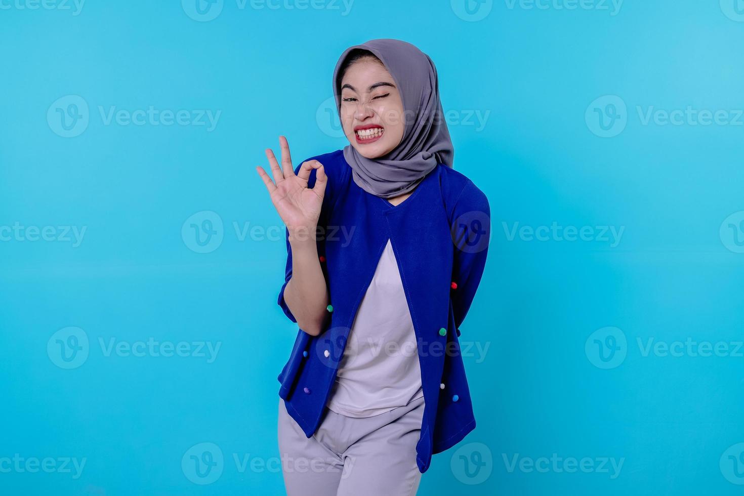 Cheerful woman with wearing hijab showing ok sign, smiling, say yes, encourage to buy something, make alright gesture photo