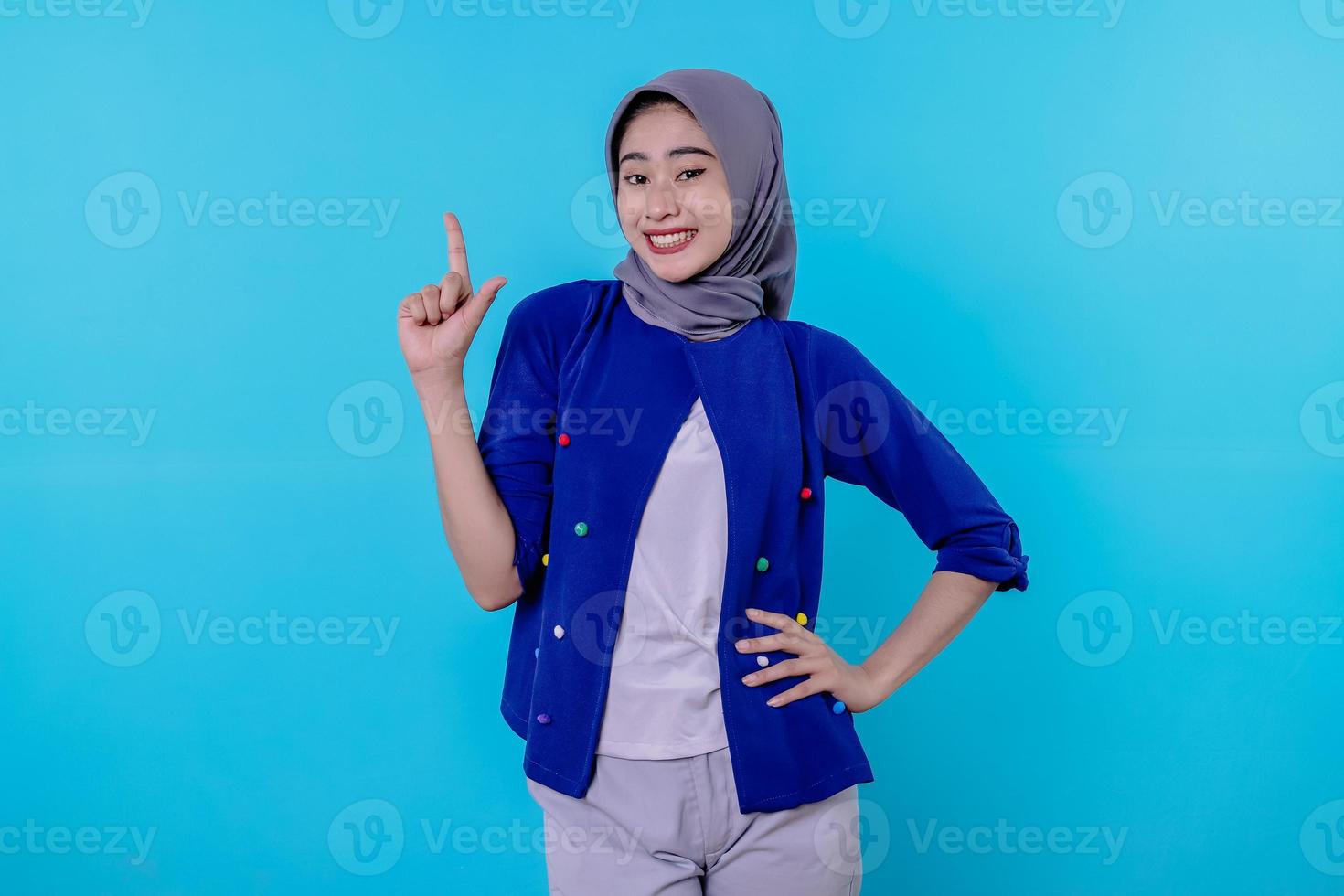 Good looking charismatic young woman with wearing hijab pointing isolated on light blue background photo