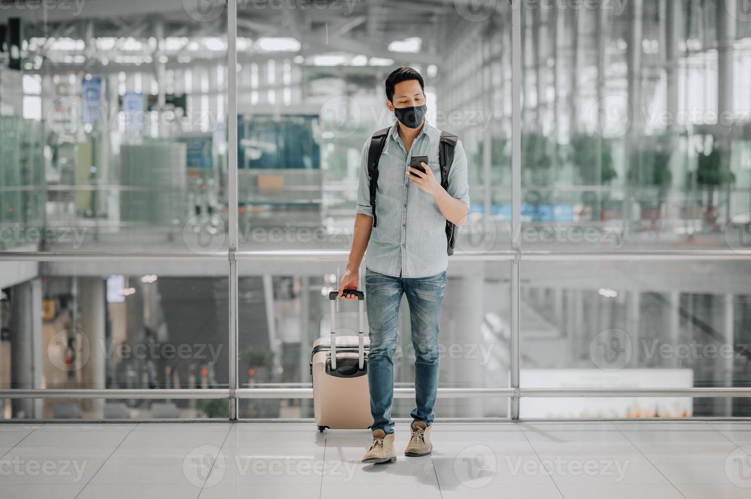 Hombre asiático con mascarilla con equipaje con smartphone foto