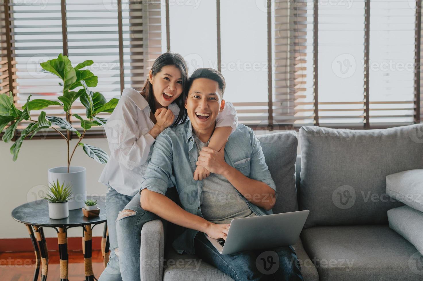Happy Asian couple using laptop on sofa at home photo