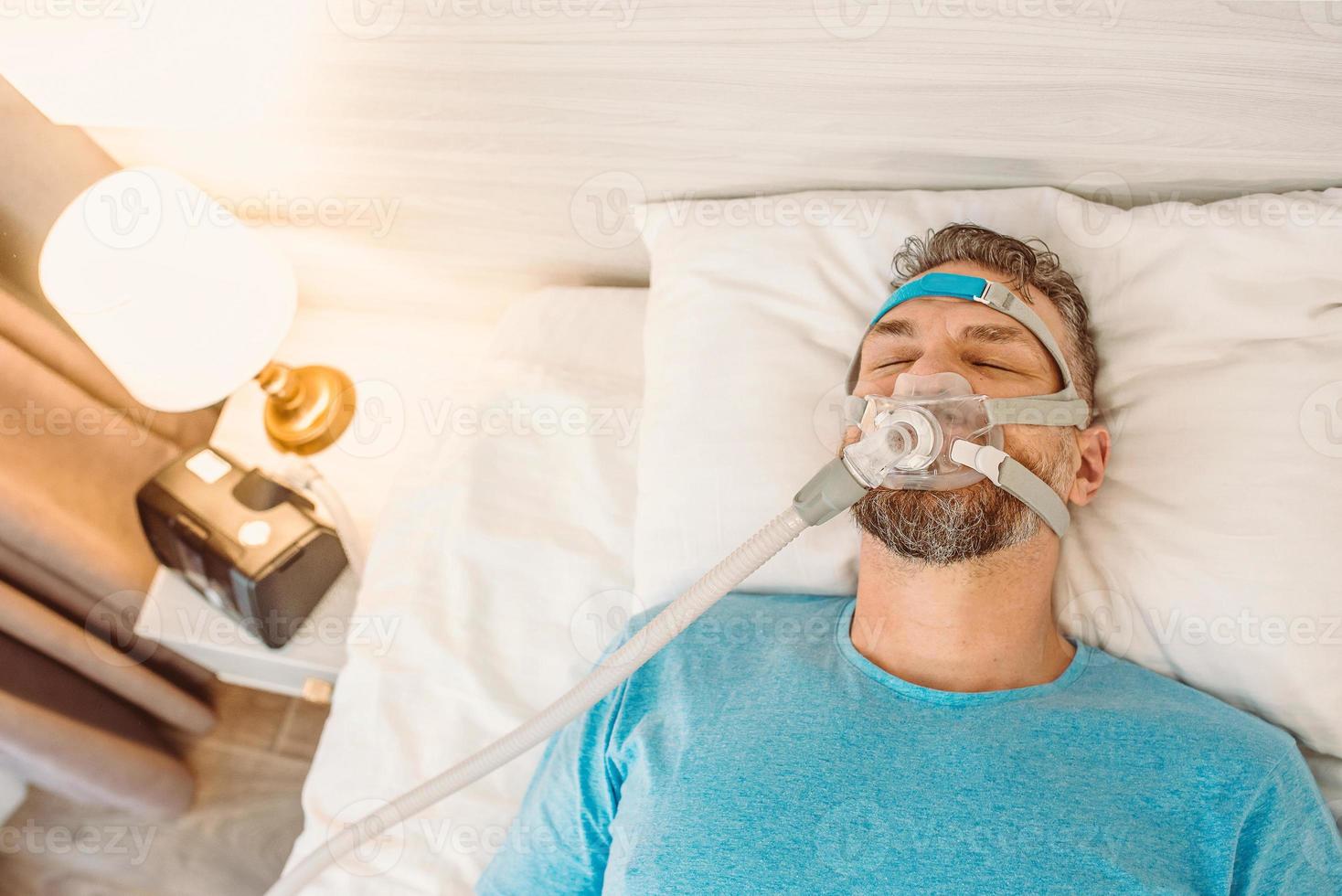 Sleeping man with chronic breathing issues considers using CPAP machine in bed. Healthcare, Obstructive sleep apnea therapy, CPAP, snoring concept photo