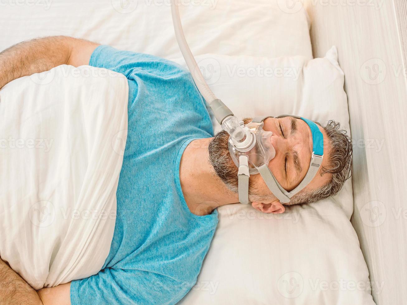 Sleeping man with chronic breathing issues considers using CPAP machine in bed. Healthcare, Obstructive sleep apnea therapy, CPAP, snoring concept photo