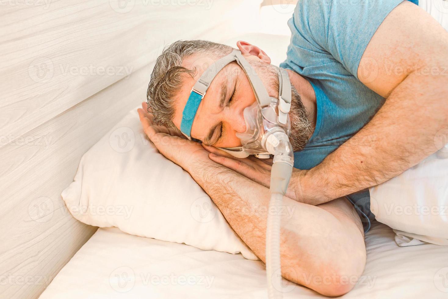 El hombre dormido con problemas respiratorios crónicos considera usar una máquina cpap en la cama. cuidado de la salud, terapia de apnea obstructiva del sueño, cpap, concepto de ronquidos foto