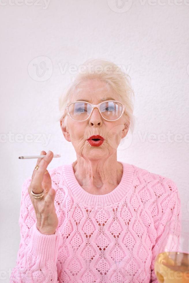 Old fashioned senior stylish woman smoking cigarette with glass of white wine. Bad habit, addiction concept photo