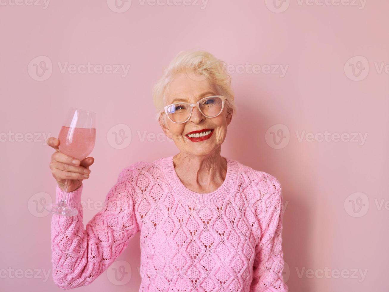 happy caucasian senior woman in cashmere pink sweater drinking rose on pink background. Celebrating, love, retirement, mature concept photo