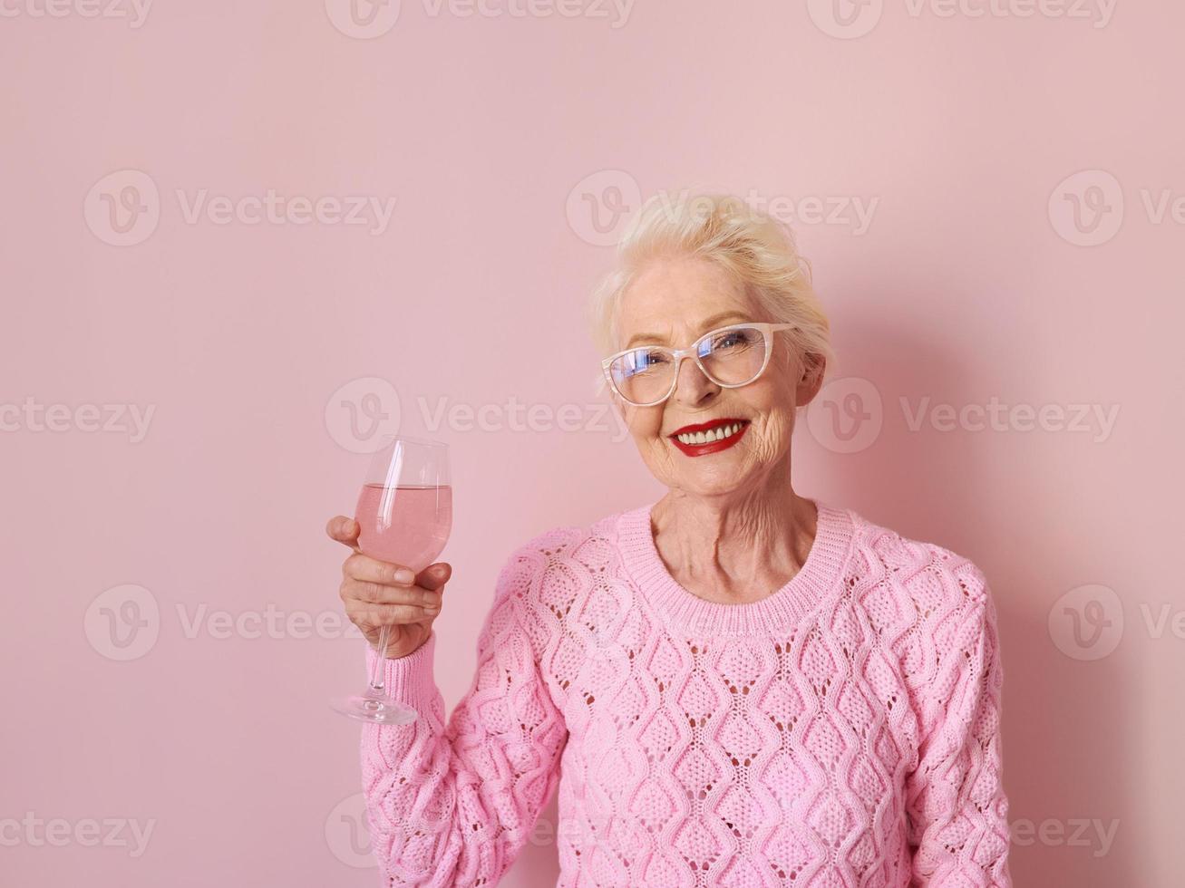 happy caucasian senior woman in cashmere pink sweater drinking rose on pink background. Celebrating, love, retirement, mature concept photo