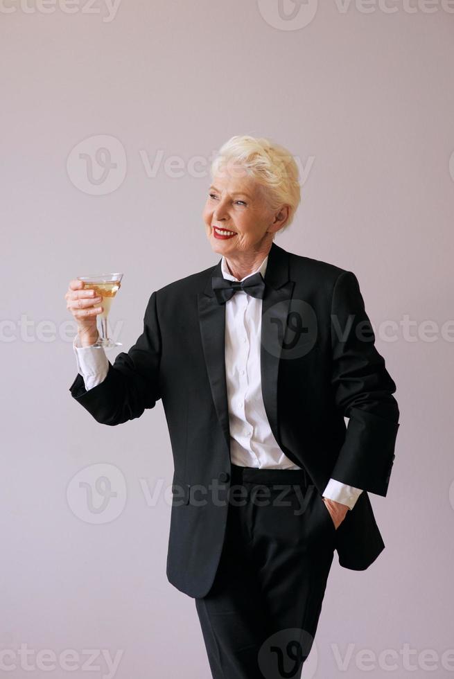 stylish mature sommelier senior woman in tuxedo with glass of sparkling wine. Fun, party, style, lifestyle, alcohol, celebration concept photo