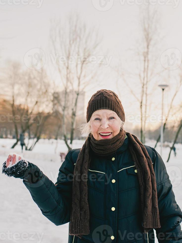 mujer mayor con sombrero y chaqueta deportiva bolas de nieve en el parque de invierno de nieve. invierno, edad, deporte, actividad, concepto de temporada foto