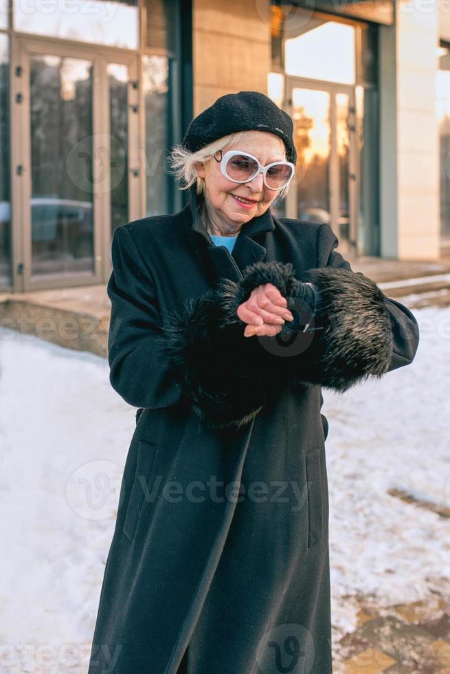 senior stylish woman in beret and elegant black coat and in medical mask walking outdoor and counting time till the end of pandemic. Lockdown, pandemic, protection concept photo