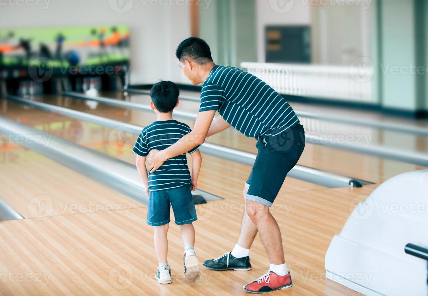 padre enseñando a su hijo a jugar a los bolos en el club de bolos foto