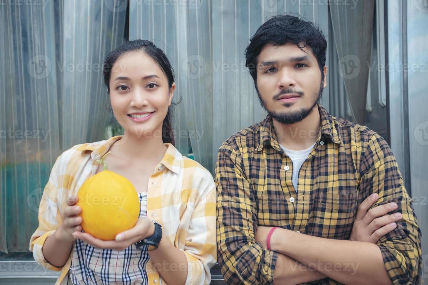 dos granjeros se paran sosteniendo un melón y sonríen felices en la granja foto