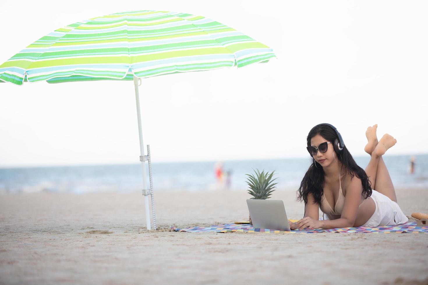 Women wearing bikinis are using laptop for work and  listen to music  at the beach in summer. photo