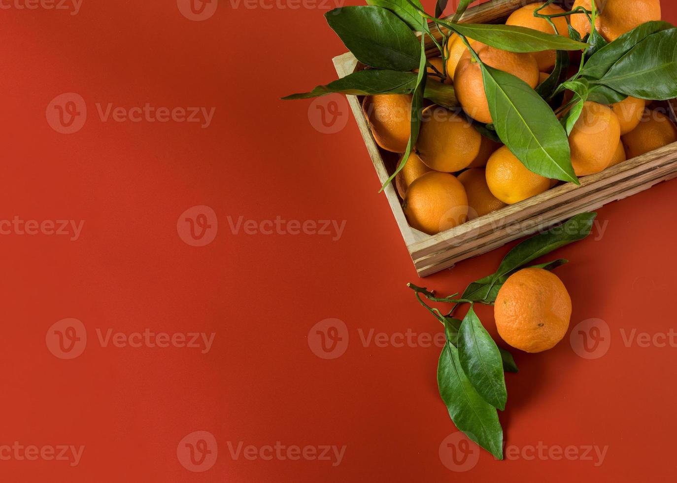 Mandarinas naranjas con follaje verde en la canasta de madera sobre fondo rojo. foto