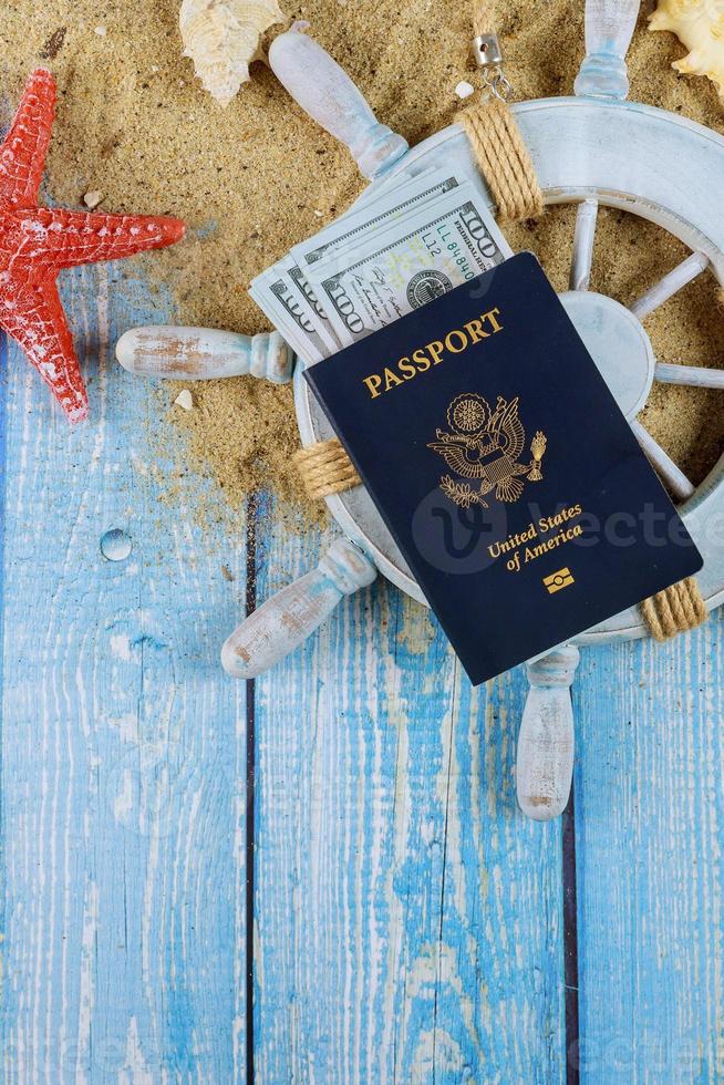 El tiempo de la rueda del capitán del marinero para viajar concepto conchas de mar en la arena de la playa más billetes de cien dólares pasaporte americano foto