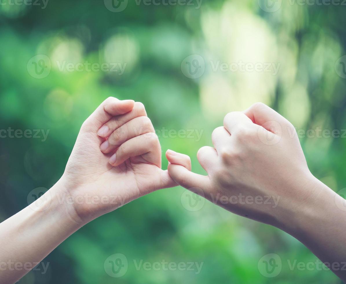 Las manos enganchan el dedo meñique del otro en el fondo de la naturaleza foto