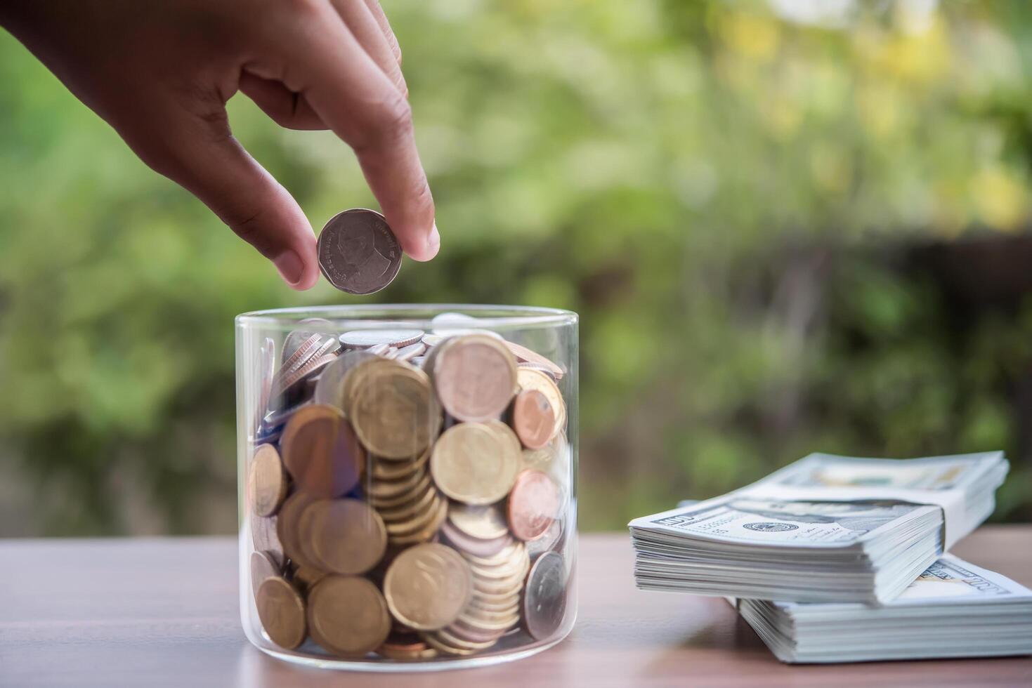 Mano poniendo monedas en el frasco con el paso de la pila de dinero crecimiento creciente ahorrando dinero foto