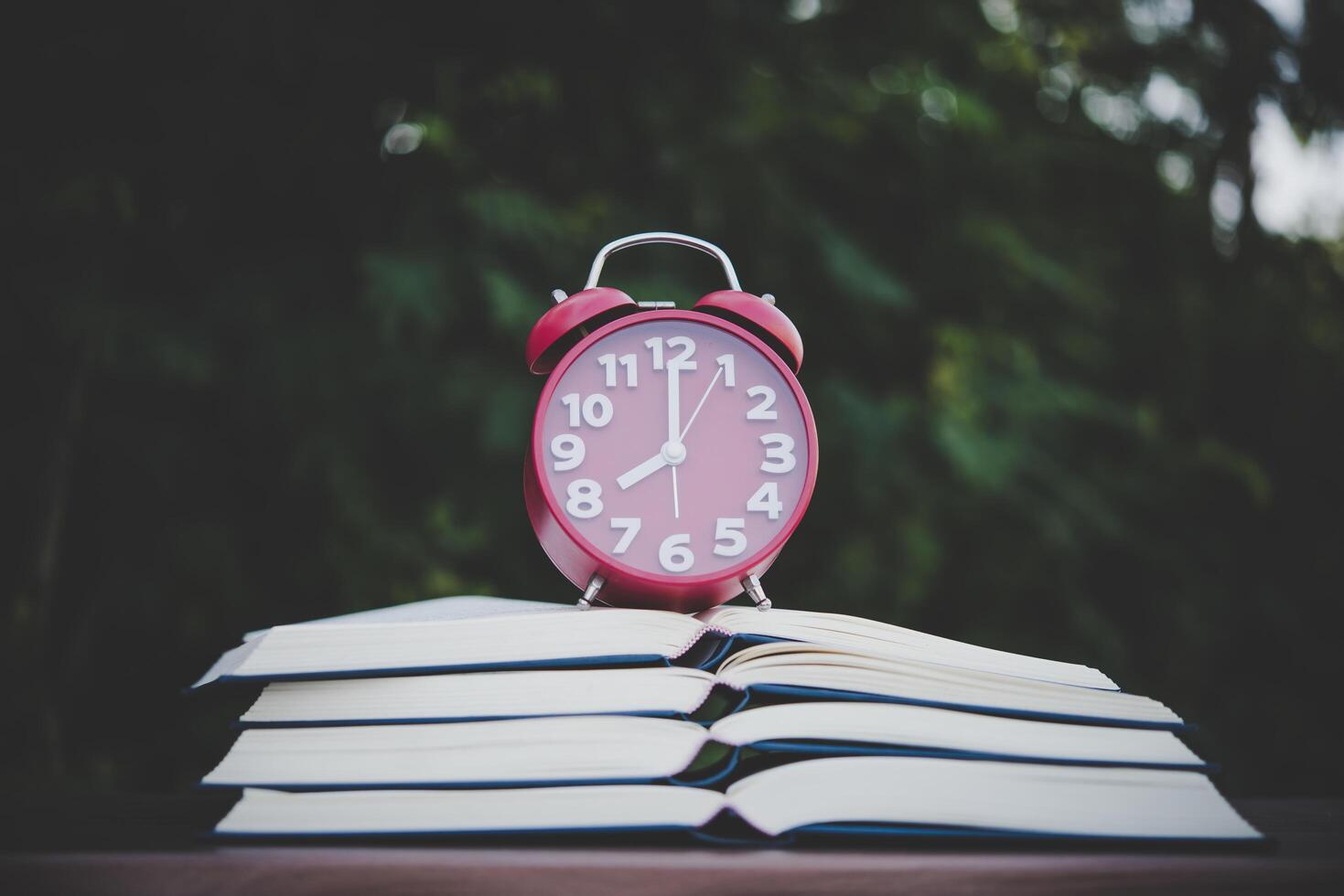 alarm clock and books on the wood table with  bokeh background. photo