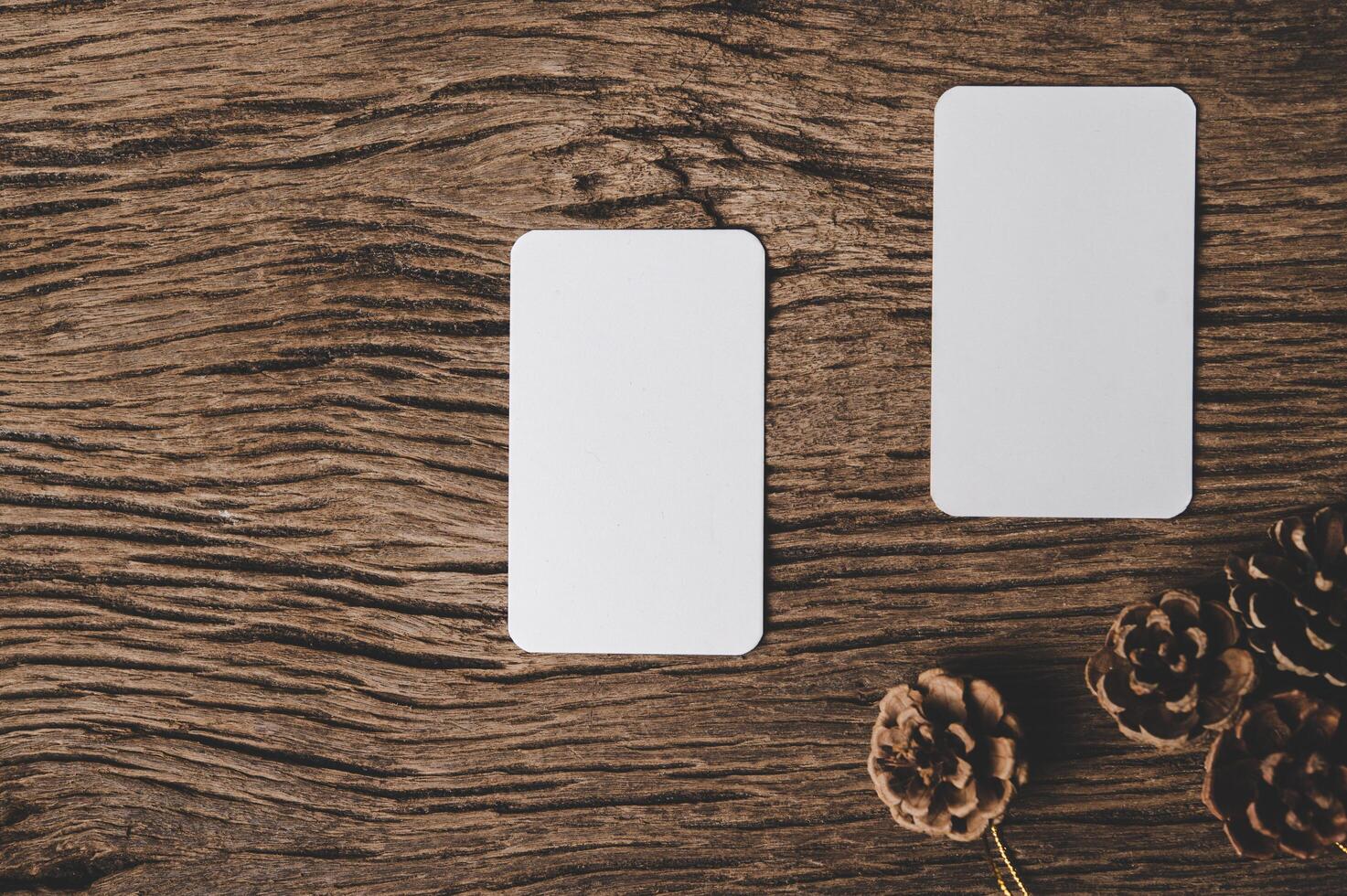 Se colocaron dos tarjetas en blanco con piñas secas sobre el fondo de madera. foto