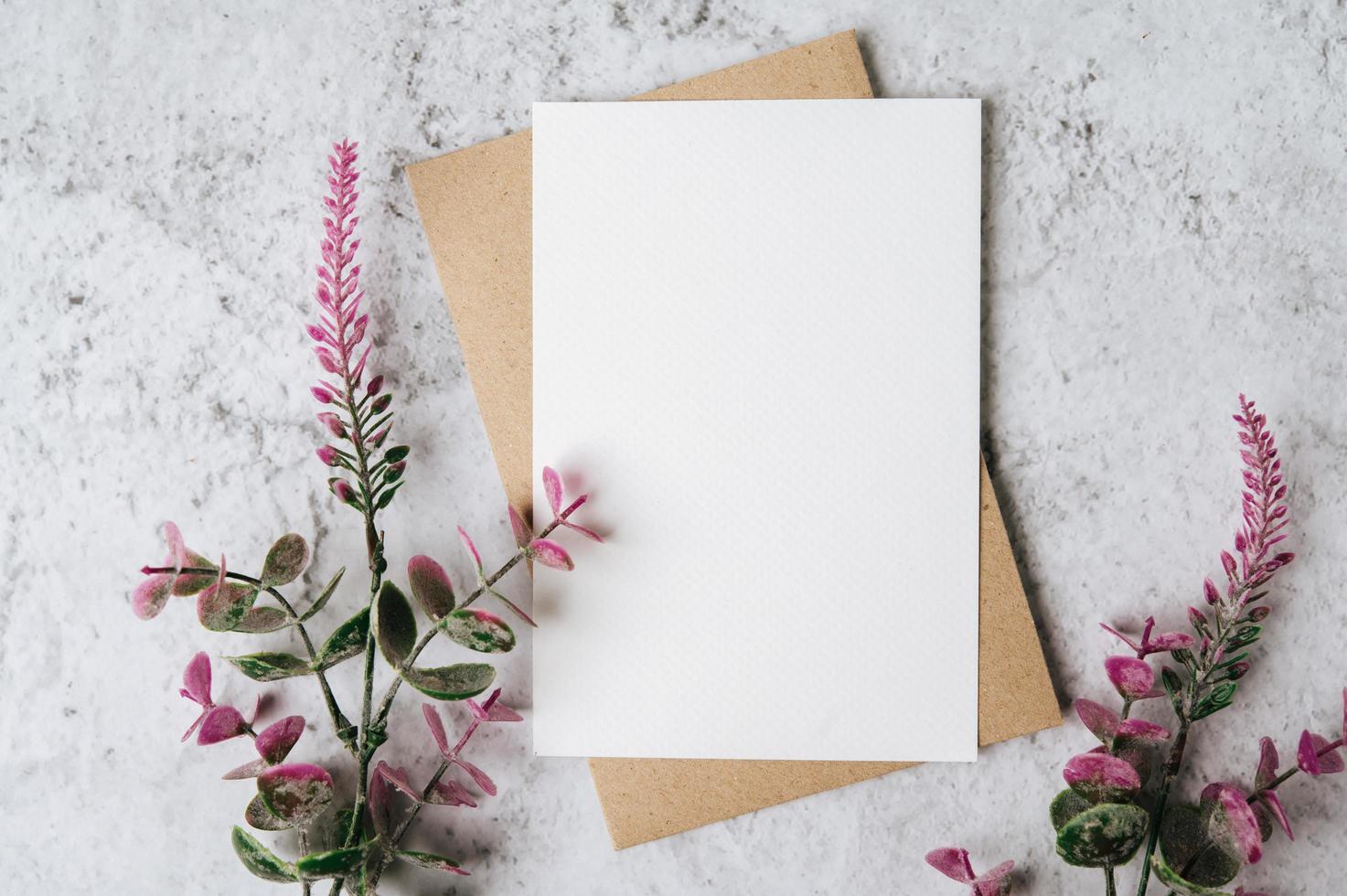 Se coloca una tarjeta en blanco con sobre y flor sobre fondo blanco. foto