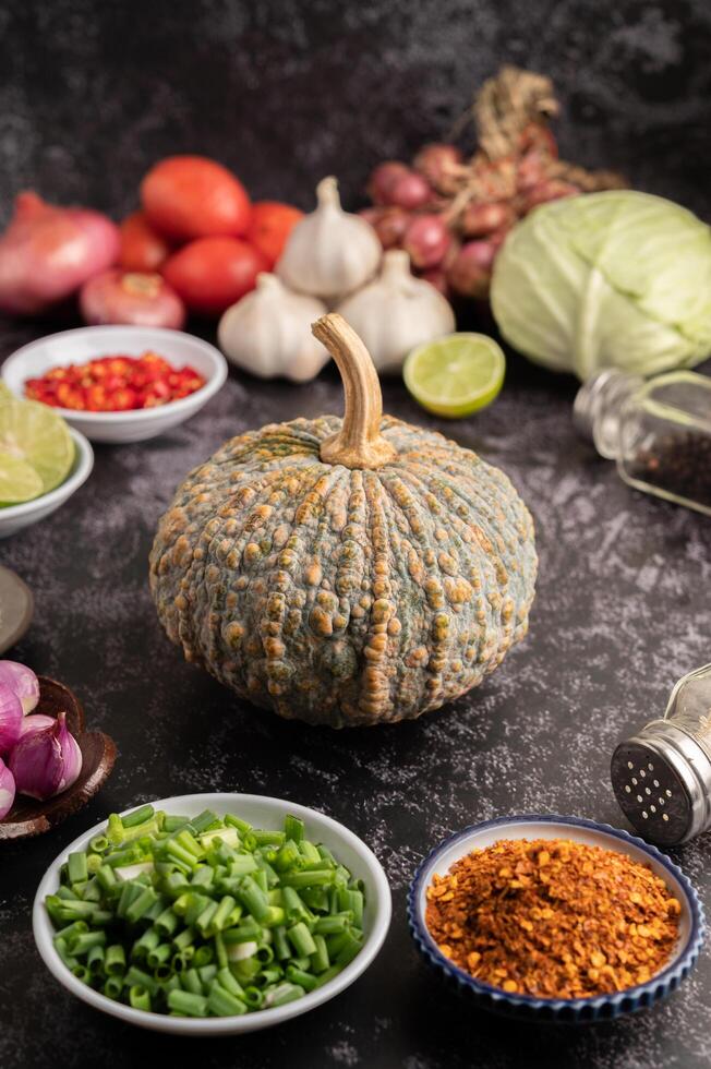 cebolletas picadas, calabaza y pimienta de cayena en una taza sobre cemento negro. foto