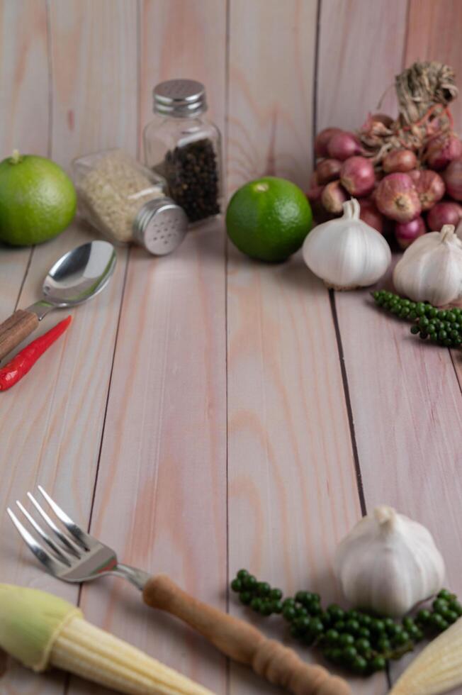 tenedor, maíz baby, ajo, pimiento fresco, lima y cebolla roja sobre un piso de madera blanca. foto
