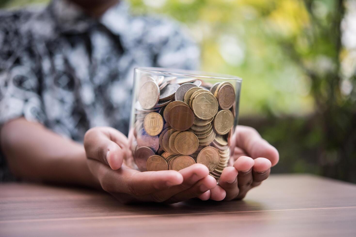 Mano poniendo monedas en el frasco con el paso de la pila de dinero crecimiento creciente ahorrando dinero foto