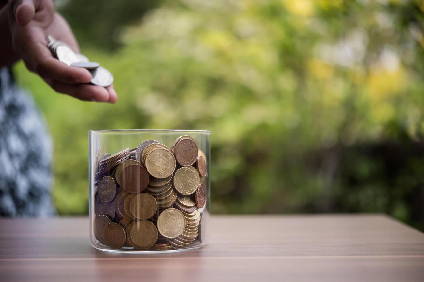 Mano poniendo monedas en el frasco con el paso de la pila de dinero crecimiento creciente ahorrando dinero foto