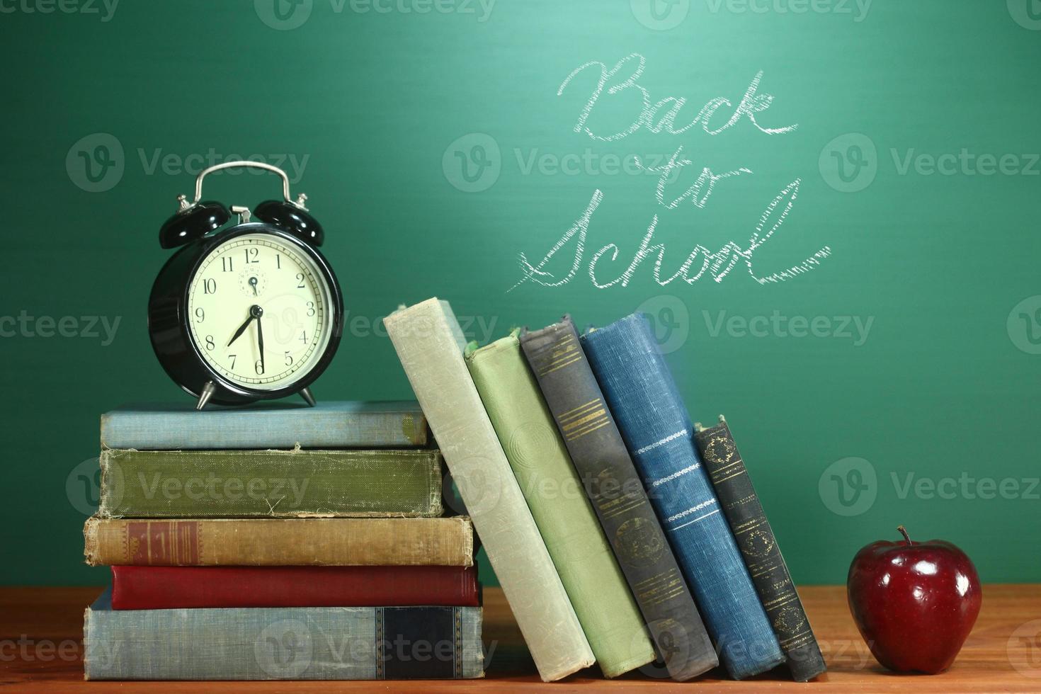 libros escolares, manzana y reloj en el escritorio en la escuela foto