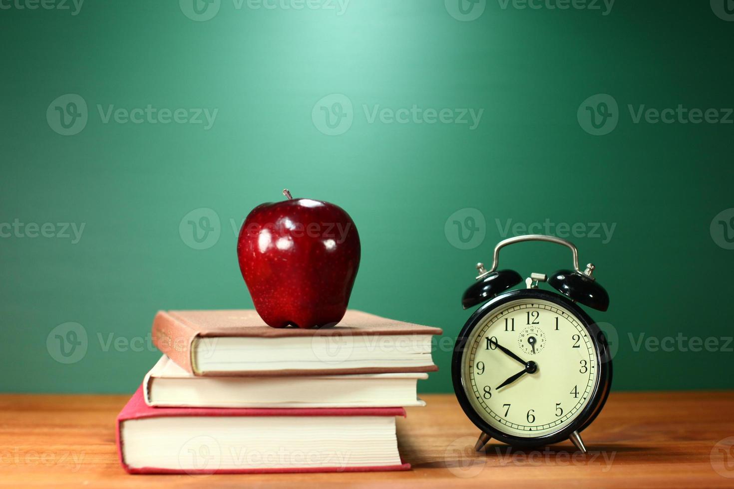 libros escolares, manzana y reloj en el escritorio en la escuela foto