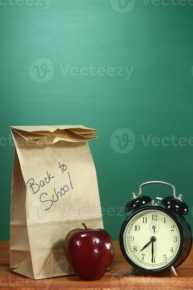 almuerzo escolar, manzana y reloj en el escritorio en la escuela foto