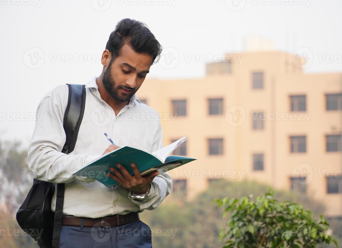 Macho joven estudiante de collage de pie fuera del campus y libro de lectura foto