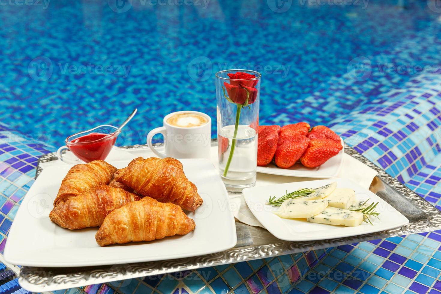 Croissants, jam, cheese, strawberry and coffee  standing on a tray on the edge of a swimming pool. photo