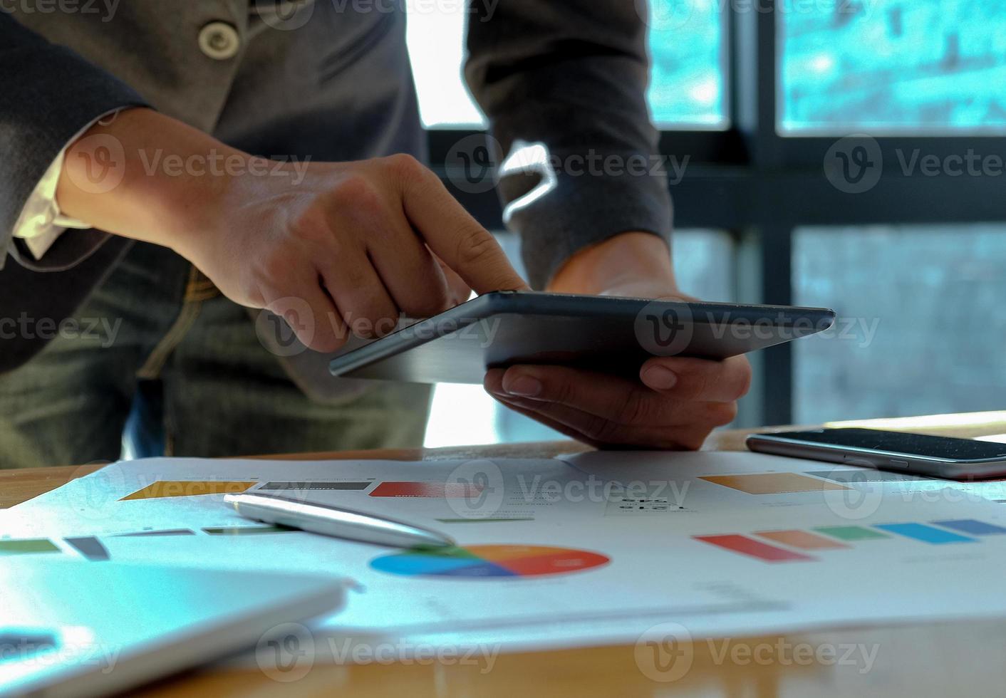 mano empresario trabaja en tableta en oficinas con gráficos sobre el escritorio. foto