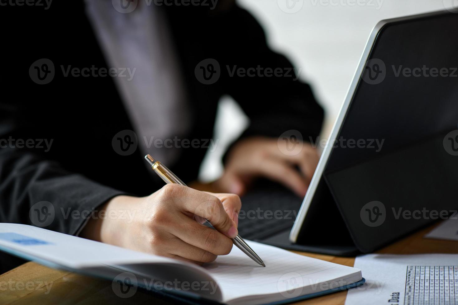 Office staff use laptop computer and note in notebook on desk in office. photo